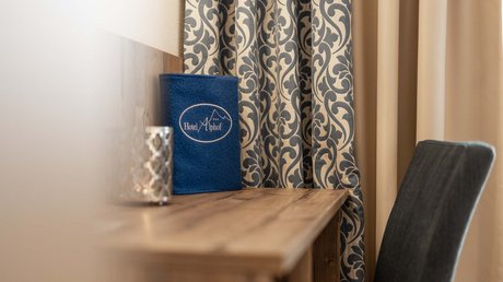 Einblicke in unser Hotel im Stubaital in Fulpmes Holztisch mit blauem Hotelordner und Mustervorhang im Zimmer