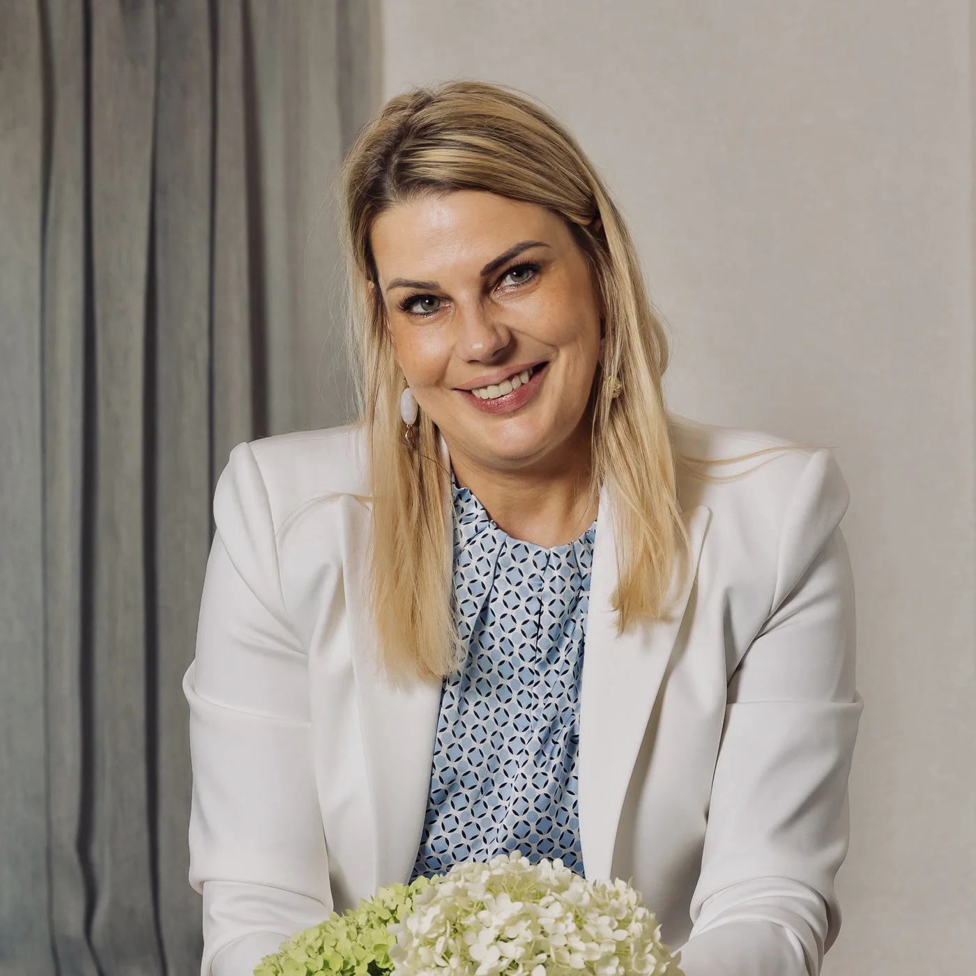 Smiling woman in a white suit holding a bouquet of flowers at a table