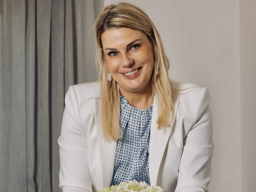 Smiling woman in a white suit holding a bouquet of flowers at a table