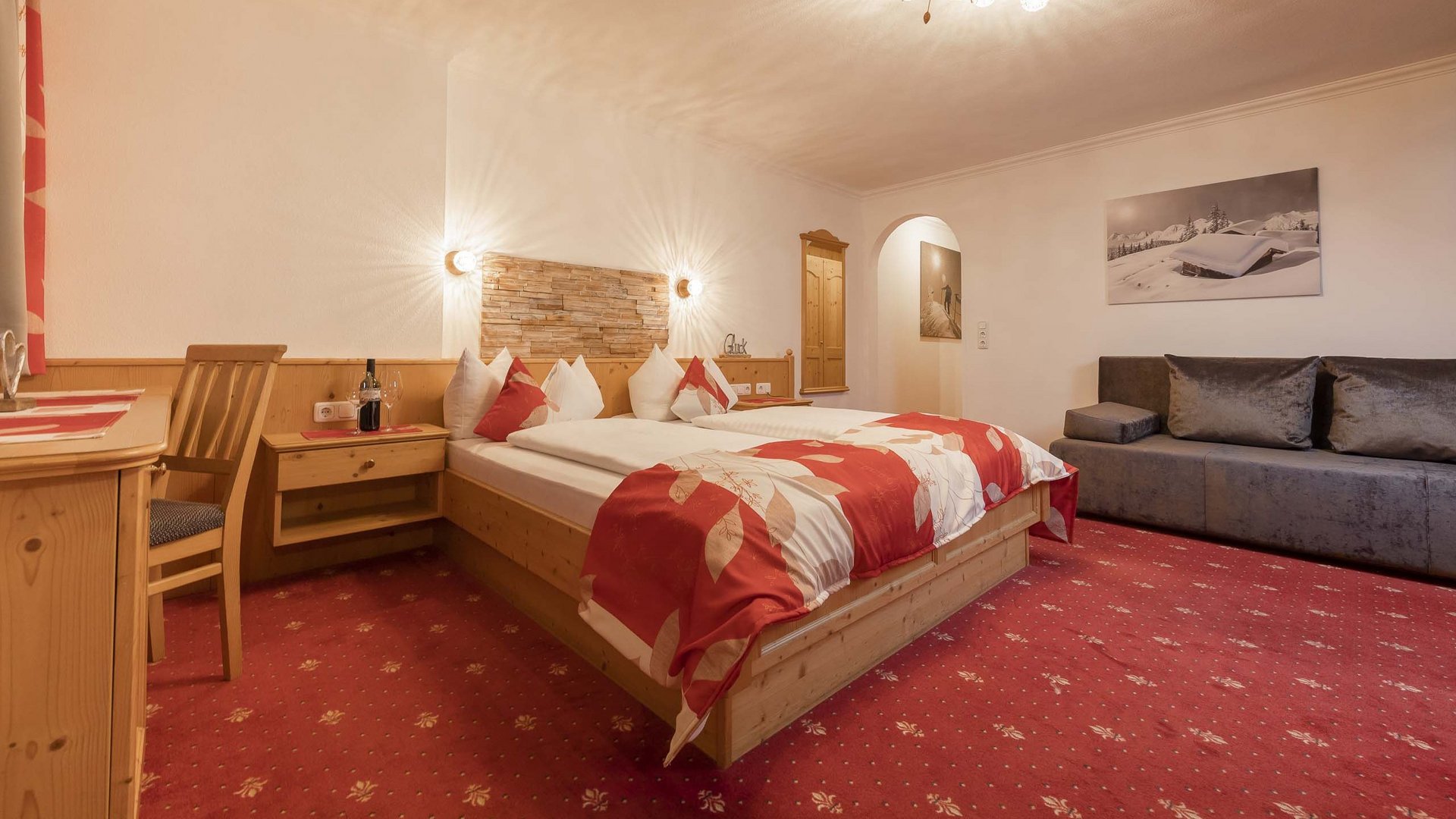 4-Sterne-Hotel Stubaital: Ihr Alphof erwartet Sie! Gemütliches Schlafzimmer mit Doppelbett, Sofa und rotem Teppich
