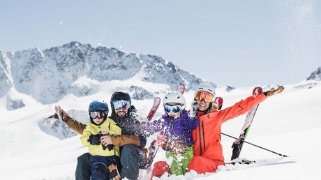 Einblicke in unser Hotel im Stubaital in Fulpmes Familie mit Skihelm und Skiausrüstung sitzt lachend im Schnee vor Bergkulisse