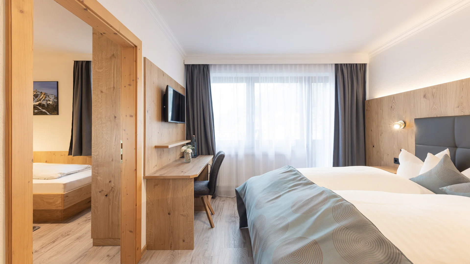 Bright hotel room with double bed, wooden furniture, desk and large window
