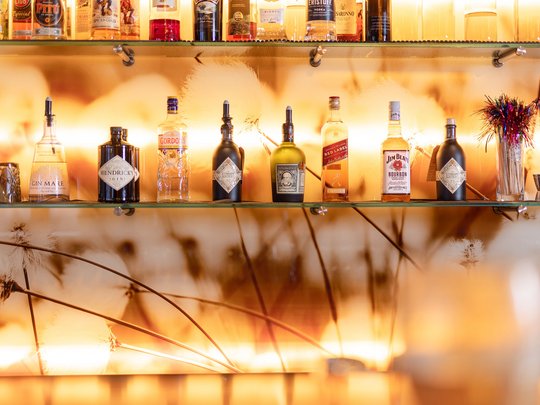 Ein feines Wellnesshotel in Fulpmes Verschiedene Spirituosenflaschen auf Glasregal vor warmem Hintergrund