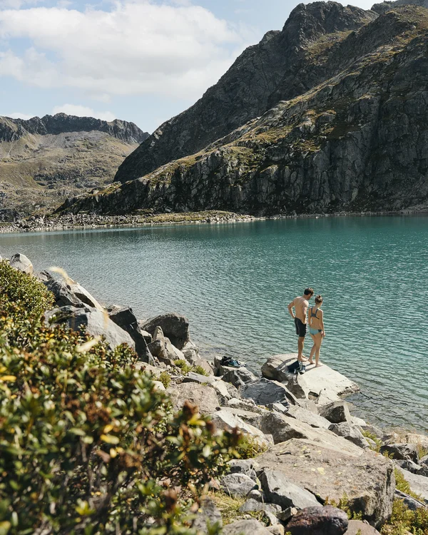 Hotel Alphof | your basecamp for walking holidays in Austria Two people beside a turquoise mountain lake surrounded by rocky peaks