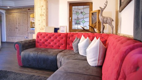 Einblicke in unser Hotel im Stubaital in Fulpmes Gemütliche rote und graue Eckcouch mit Zierkissen und Hirschdekoration im Wohnzimmer