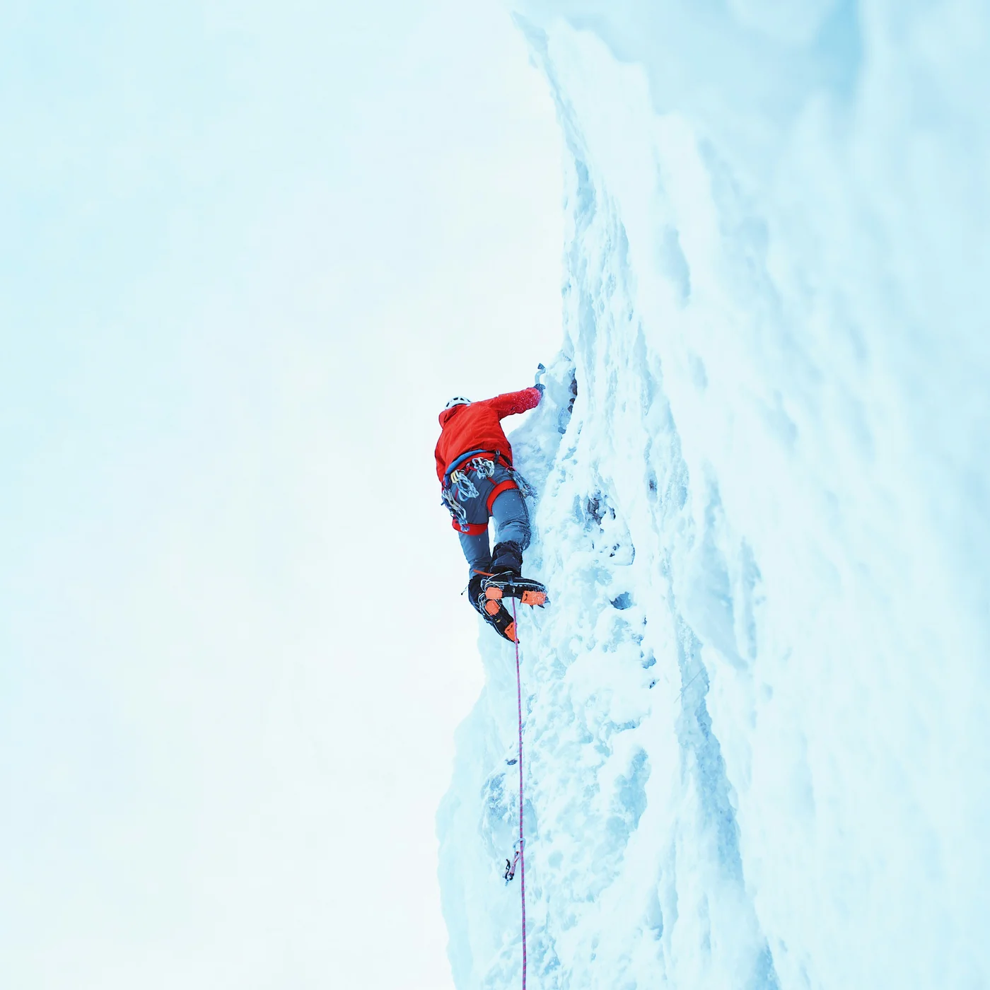 Ice climber in a red jacket scaling a steep ice wall