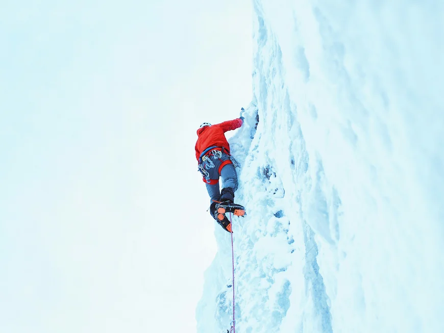 Ice climber in a red jacket scaling a steep ice wall