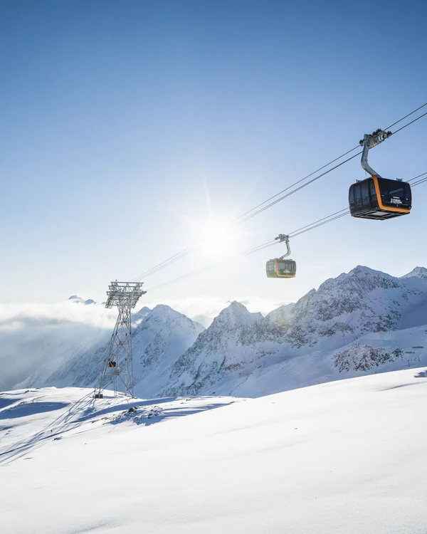 Gondolas above snow-covered mountains in bright sunshine