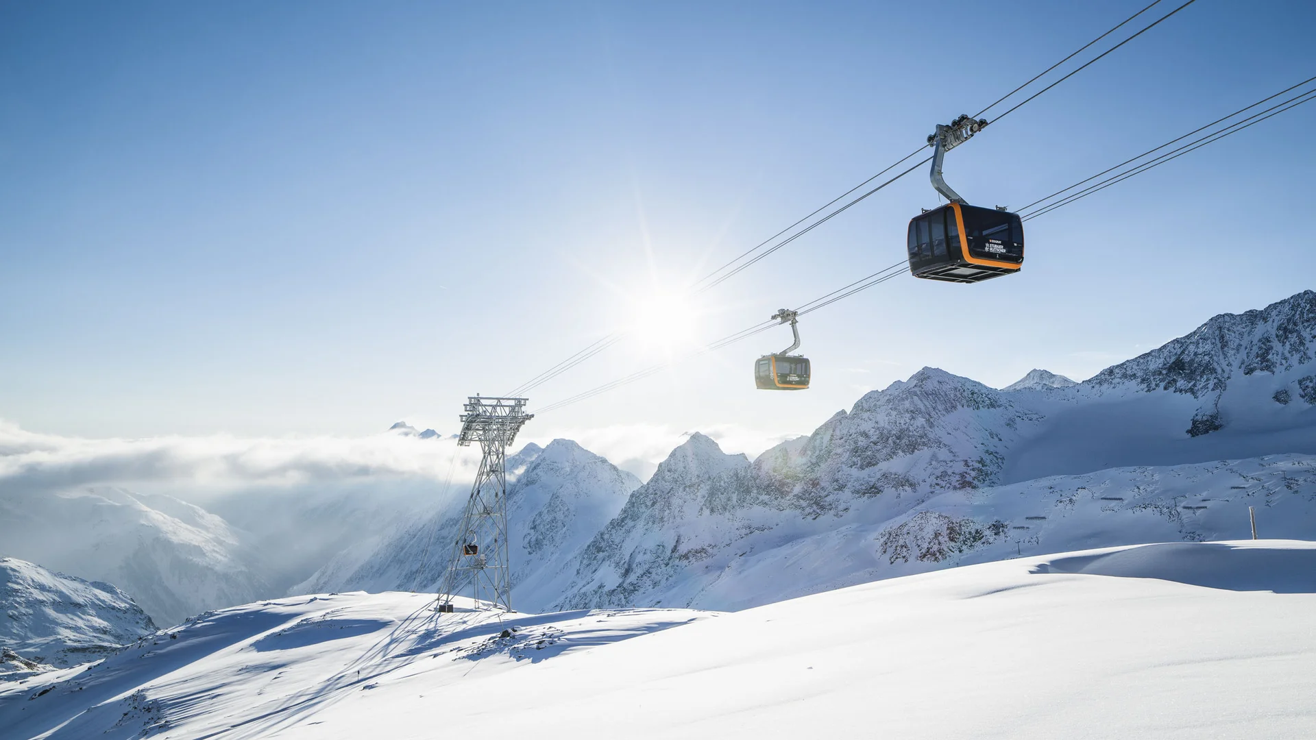 Gondolas above snow-covered mountains in bright sunshine