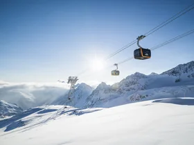 Gondolas above snow-covered mountains in bright sunshine