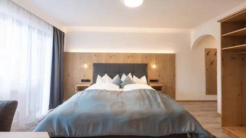 Bright bedroom with double bed, wood paneling and open wardrobe