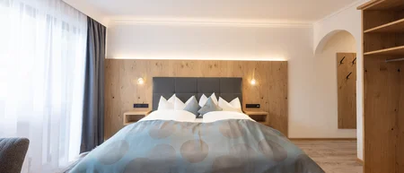 Bright bedroom with double bed, wood paneling and open wardrobe