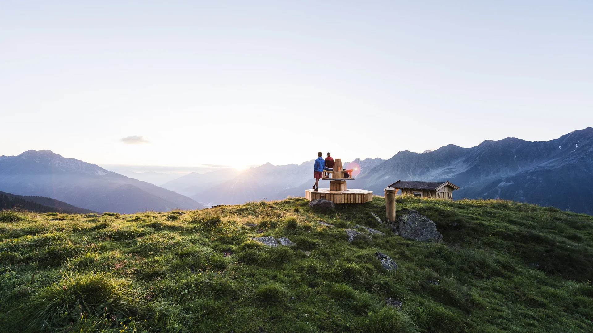 Three people enjoy sunset on a mountain meadow overlooking the Alps