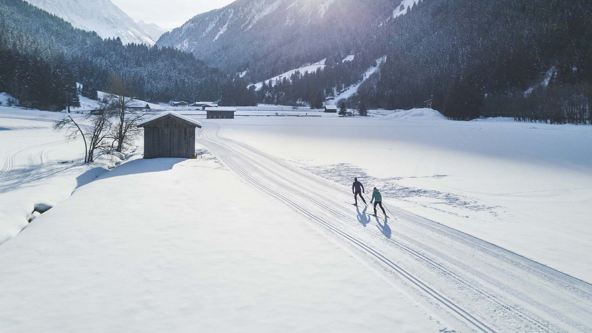 Winterurlaub in Tirol: Hotel Alphof in Fulpmes Zwei Langläufer auf verschneiter Strecke vor Bergen im Sonnenschein