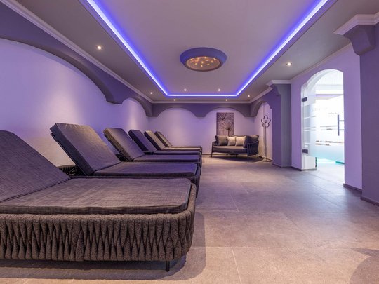 Unser Wellnesshotel im Stubaital Entspannungsbereich mit Liegen und Sofa in einem modernen Wellnessraum mit blauer Beleuchtung