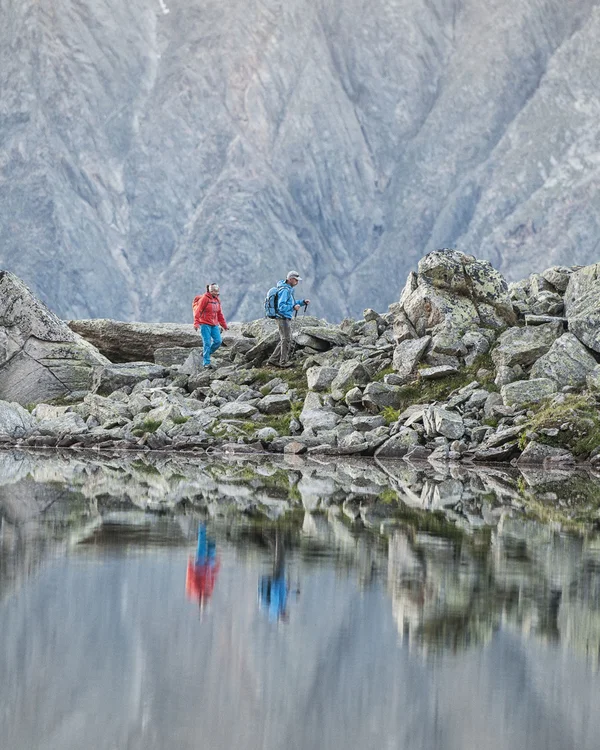 Alphof in Fulpmes, Tyrol | Attractions Two hikers by a rocky mountain lake reflected in the water