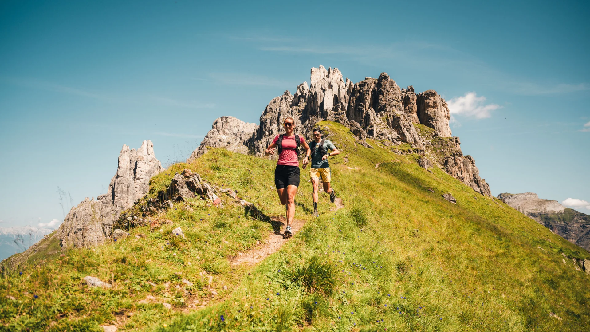 Two hikers on a mountain trail in front of a rugged rock formation