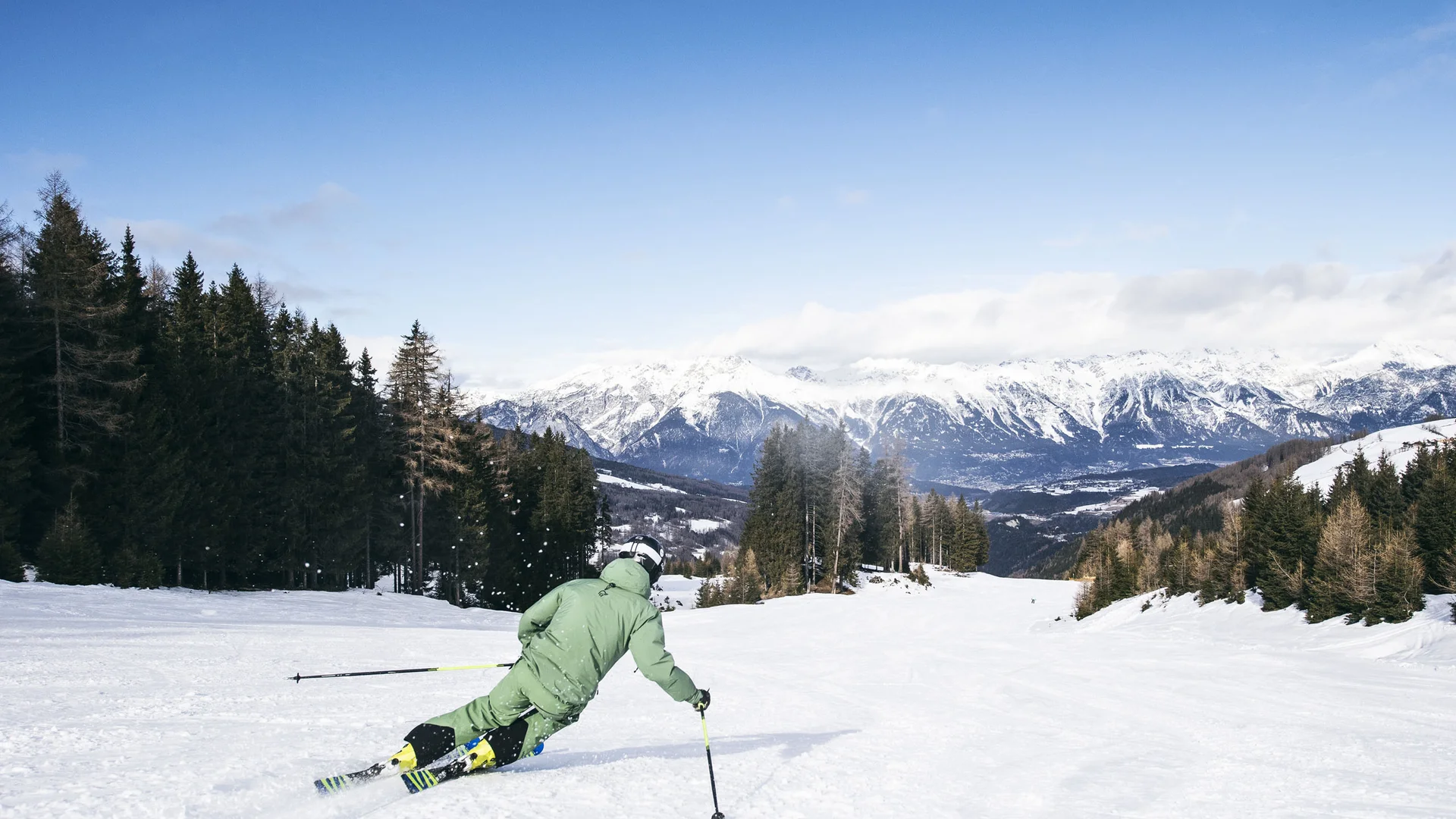 Skier descending a snowy slope with a mountain panorama
