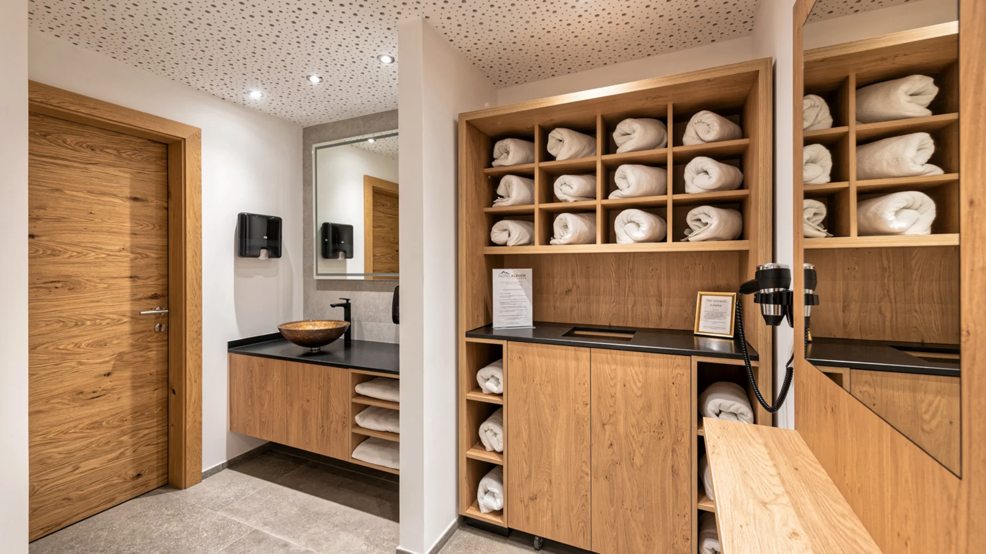 Modern changing room with wooden cabinets, folded towels, sink and mirror