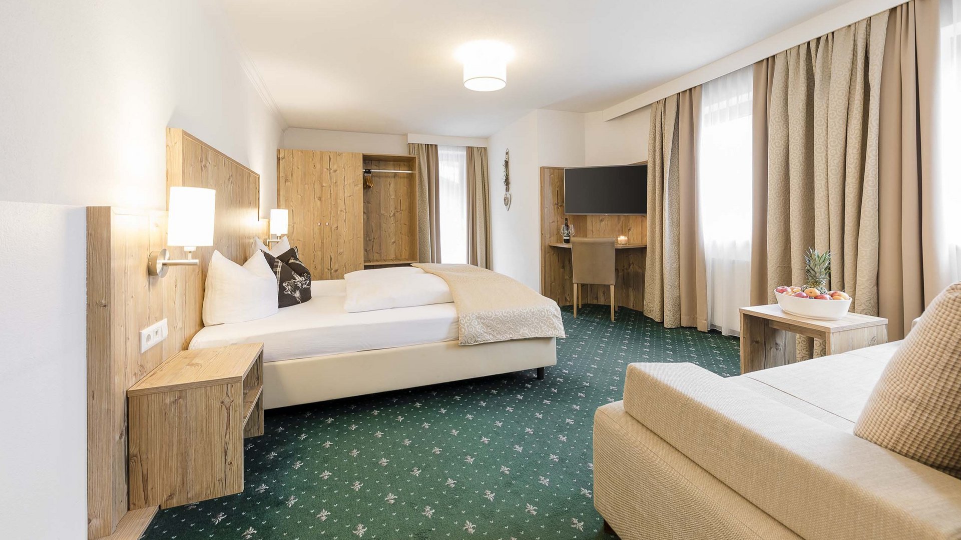 4-Sterne-Hotel Stubaital: Ihr Alphof erwartet Sie! Helles Hotelzimmer mit Doppelbett, Sitzbereich, TV und großem Fenster