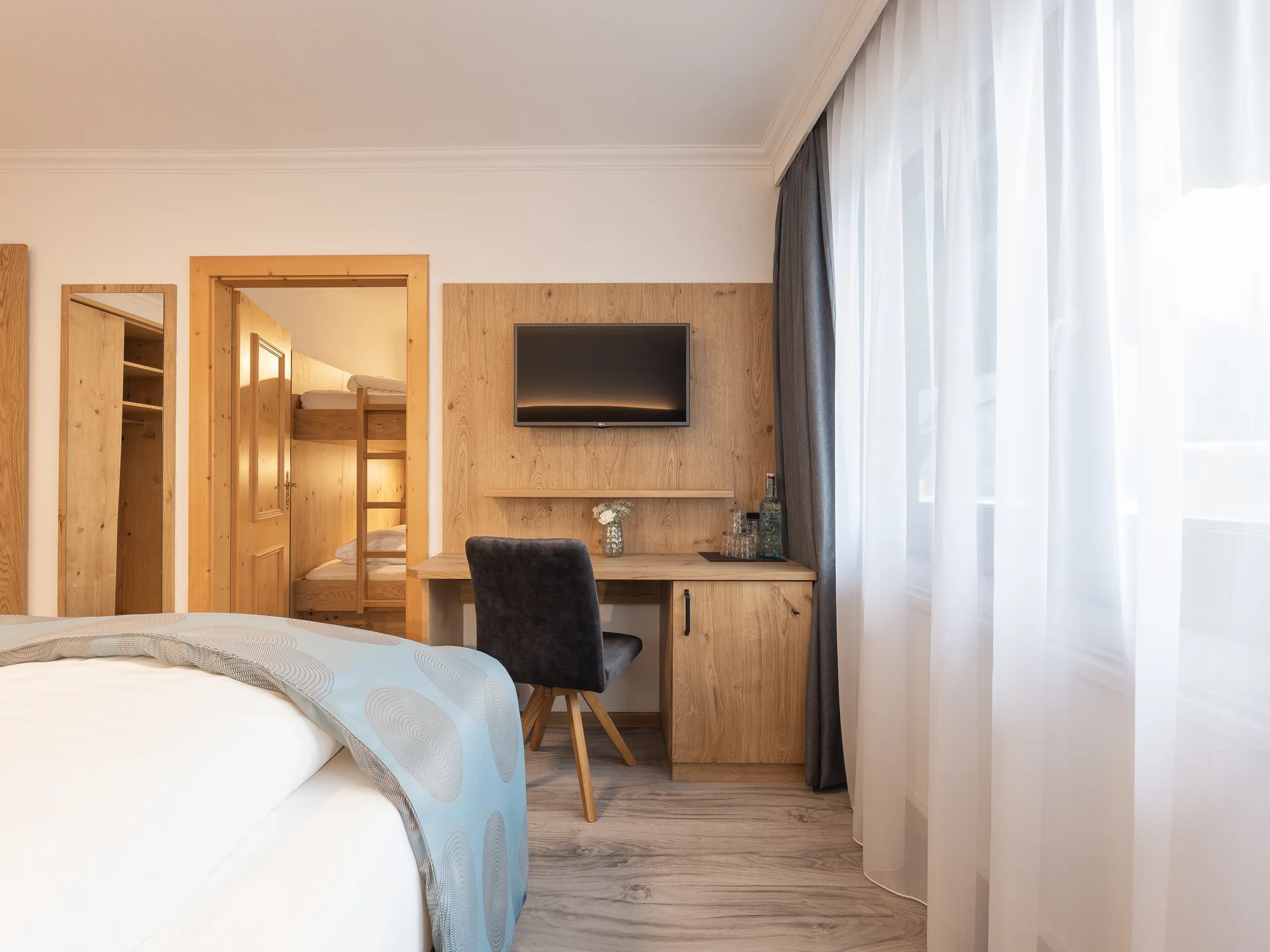 Der Alphof | Ihr Hotel in Fulpmes Helles Hotelzimmer mit Bett, Schreibtisch, Fernseher und Fensterfront