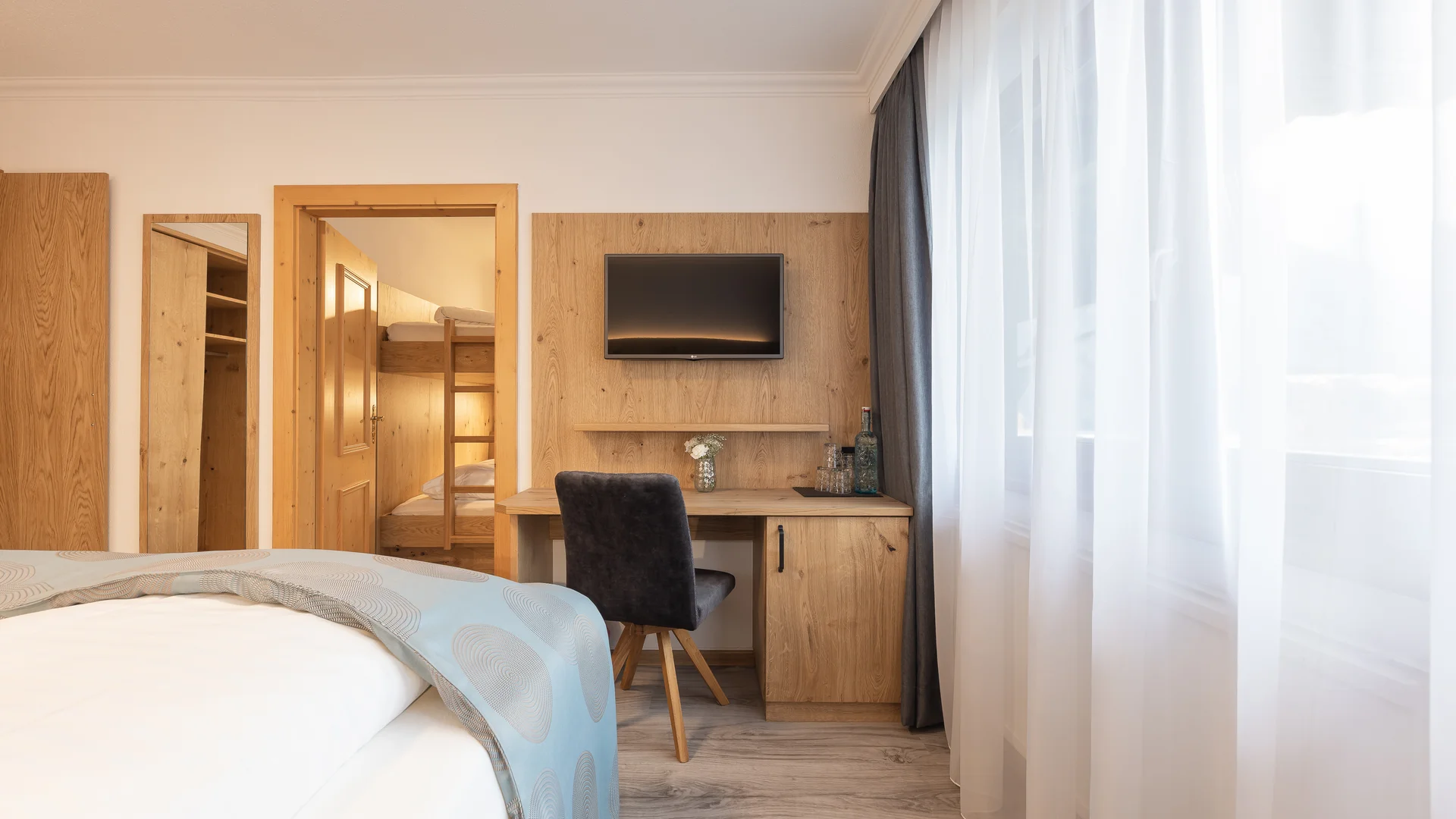 Bright hotel room with bed, desk, television and floor-to-ceiling windows