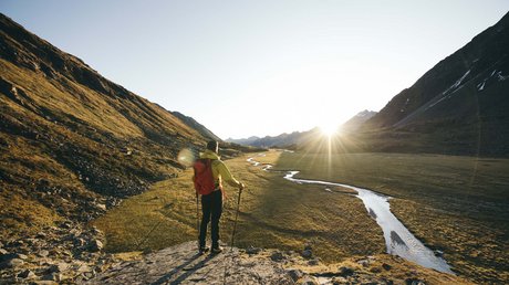 Einblicke in unser Hotel im Stubaital in Fulpmes Wanderer mit rotem Rucksack blickt auf ein Tal mit Bach bei Sonnenuntergang