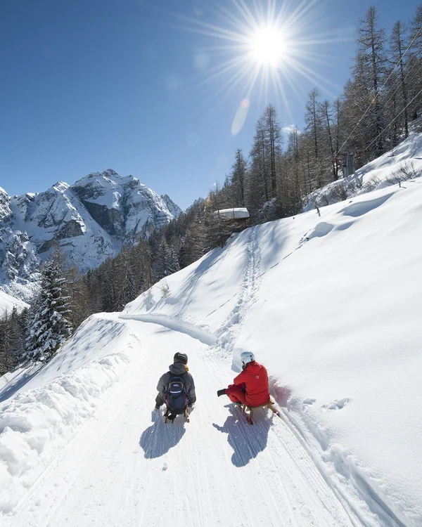 Two people hiking through snowy mountains beneath a bright blue sky