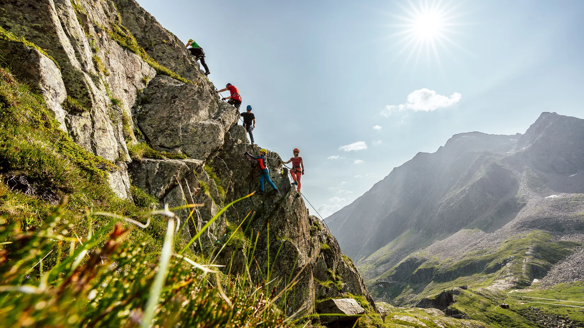 Four climbers on a rock face against an alpine mountain landscape