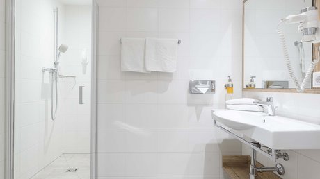 Einblicke in unser Hotel im Stubaital in Fulpmes Helles Badezimmer mit Dusche, Waschbecken, großem Spiegel und Handtüchern