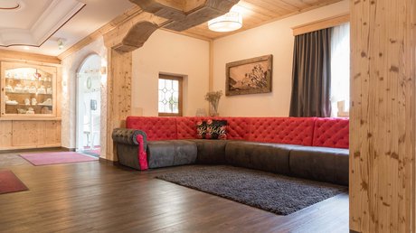 Einblicke in unser Hotel im Stubaital in Fulpmes Gemütliches Wohnzimmer mit rotem und grauem Ecksofa und Holzbalkendecke