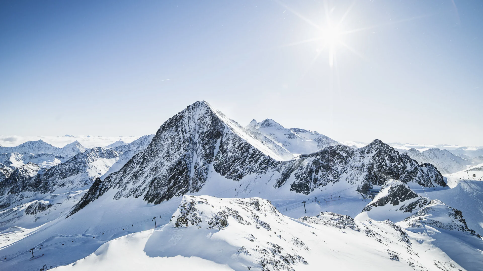 Snow-covered mountain landscape with a prominent peak and bright sun