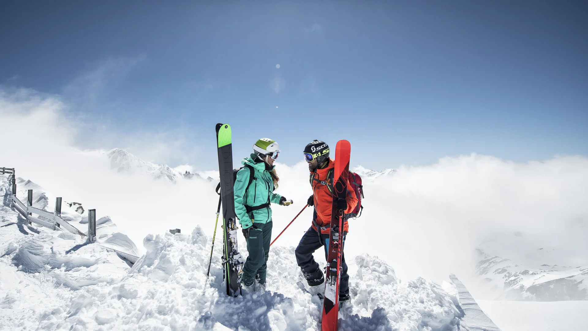 Two skiers with skis in the snowy high mountains beneath a blue sky