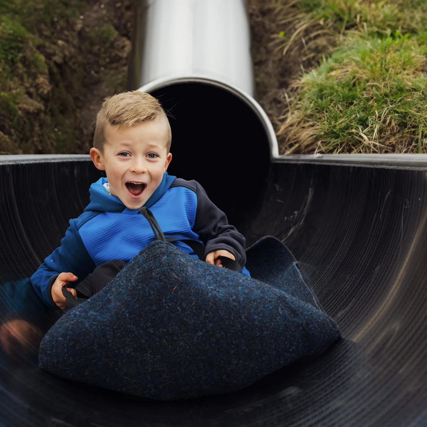 Boy in a blue top riding in a black tube through a slide