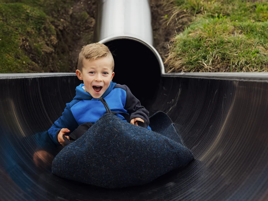 Boy in a blue top riding in a black tube through a slide