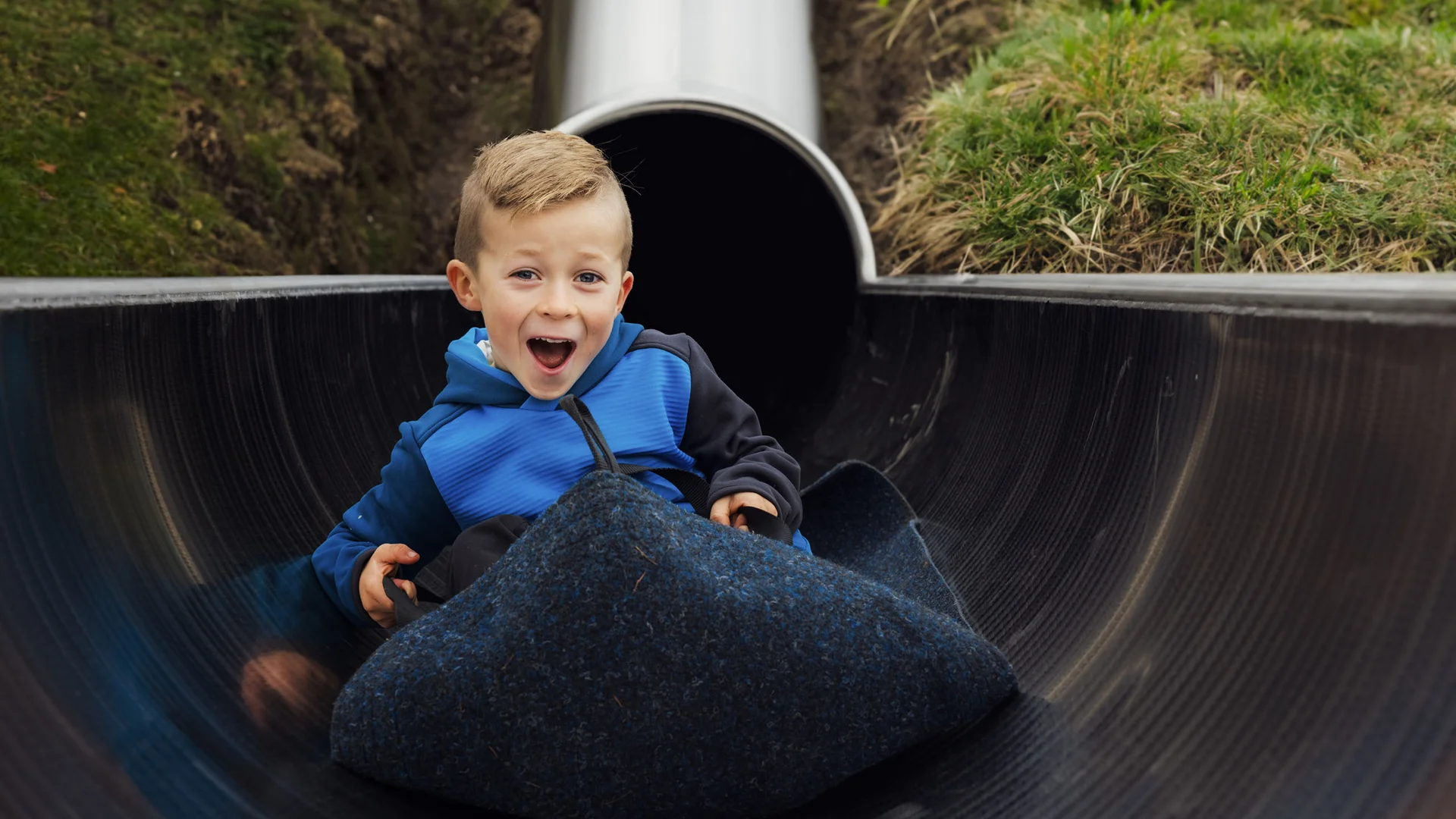 Boy in a blue top riding in a black tube through a slide