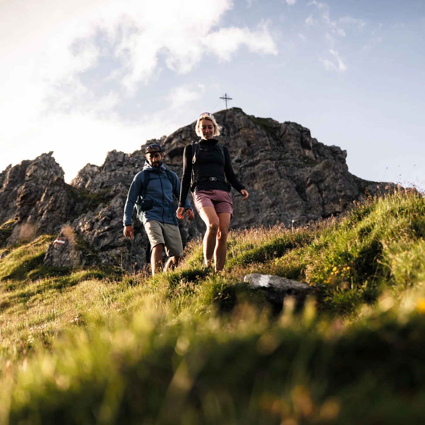 Hotel Alphof | your basecamp for walking holidays in Austria Two hikers walk across a meadow in front of a rocky mountain landscape