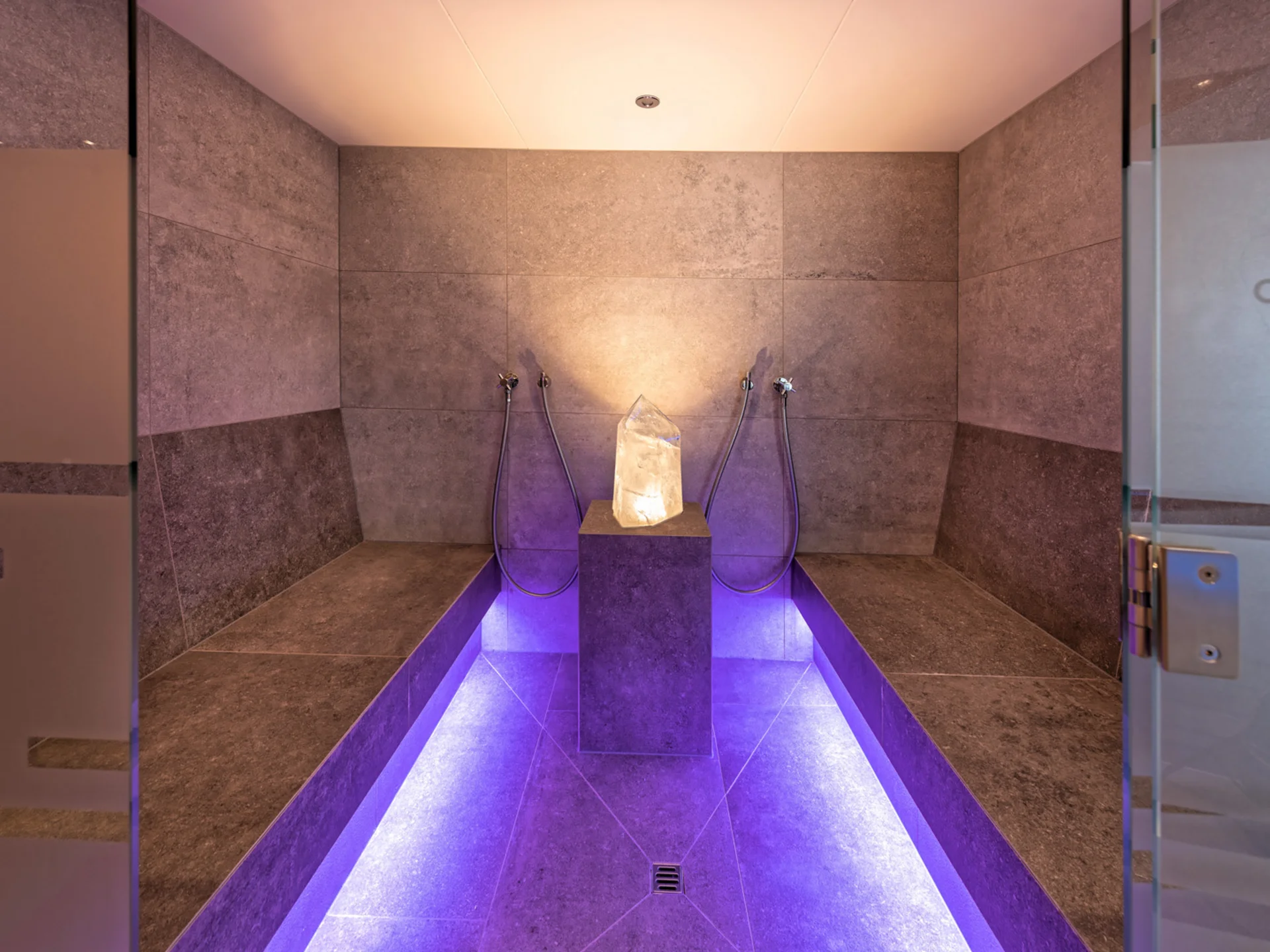 The modern AlpSpa at your spa hotel in Tyrol Steam room with natural stone walls, benches and purple lighting