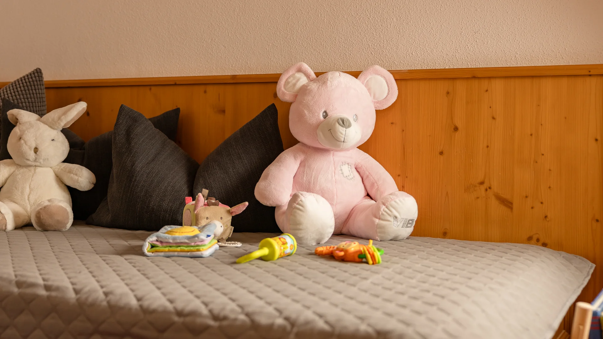 Bed with a pink teddy bear, plush rabbit, cushions and colorful toys