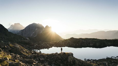 Einblicke in unser Hotel im Stubaital in Fulpmes Person steht an einem Bergsee mit Sonnenaufgang und Bergen im Hintergrund