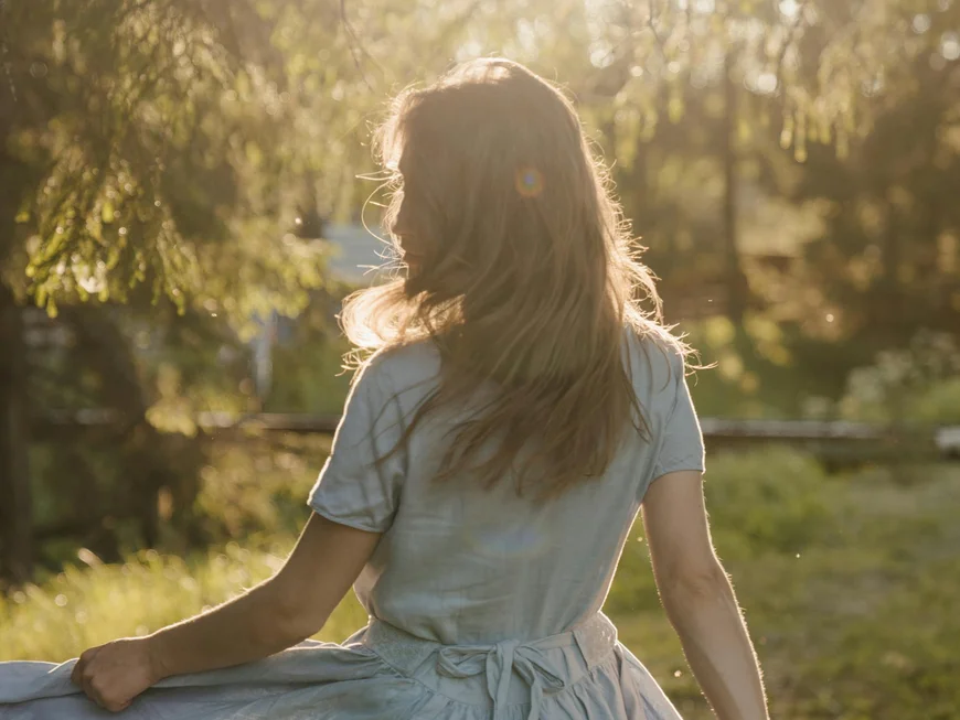 Rear view of a woman in a light dress in sunlight in the forest