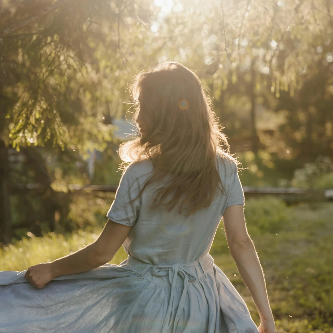 Rear view of a woman in a light dress in sunlight in the forest