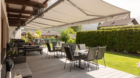 Einblicke in unser Hotel im Stubaital in Fulpmes Terrasse mit Tischen, Stühlen, Markise und Blick auf Garten und Häuser