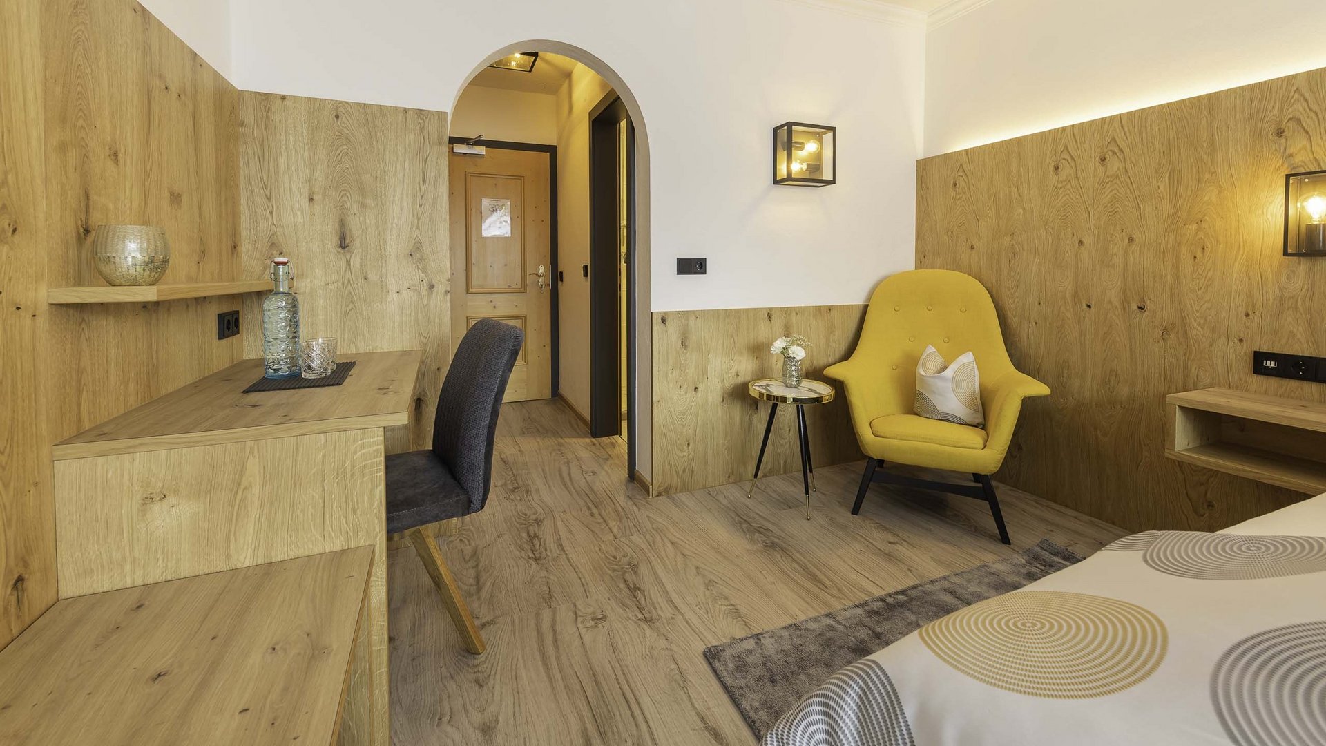 4-Sterne-Hotel Stubaital: Ihr Alphof erwartet Sie! Heller Hotelzimmer mit gelbem Sessel, Holzmöbeln und Schreibtisch mit Stuhl