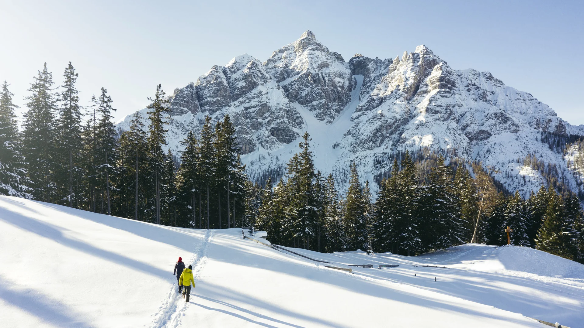 Two hikers on a snowy path before a majestic mountain landscape