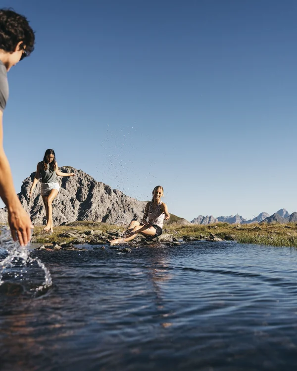Alphof in Fulpmes, Tyrol | Attractions Three people wade in a mountain lake with alpine peaks in the background