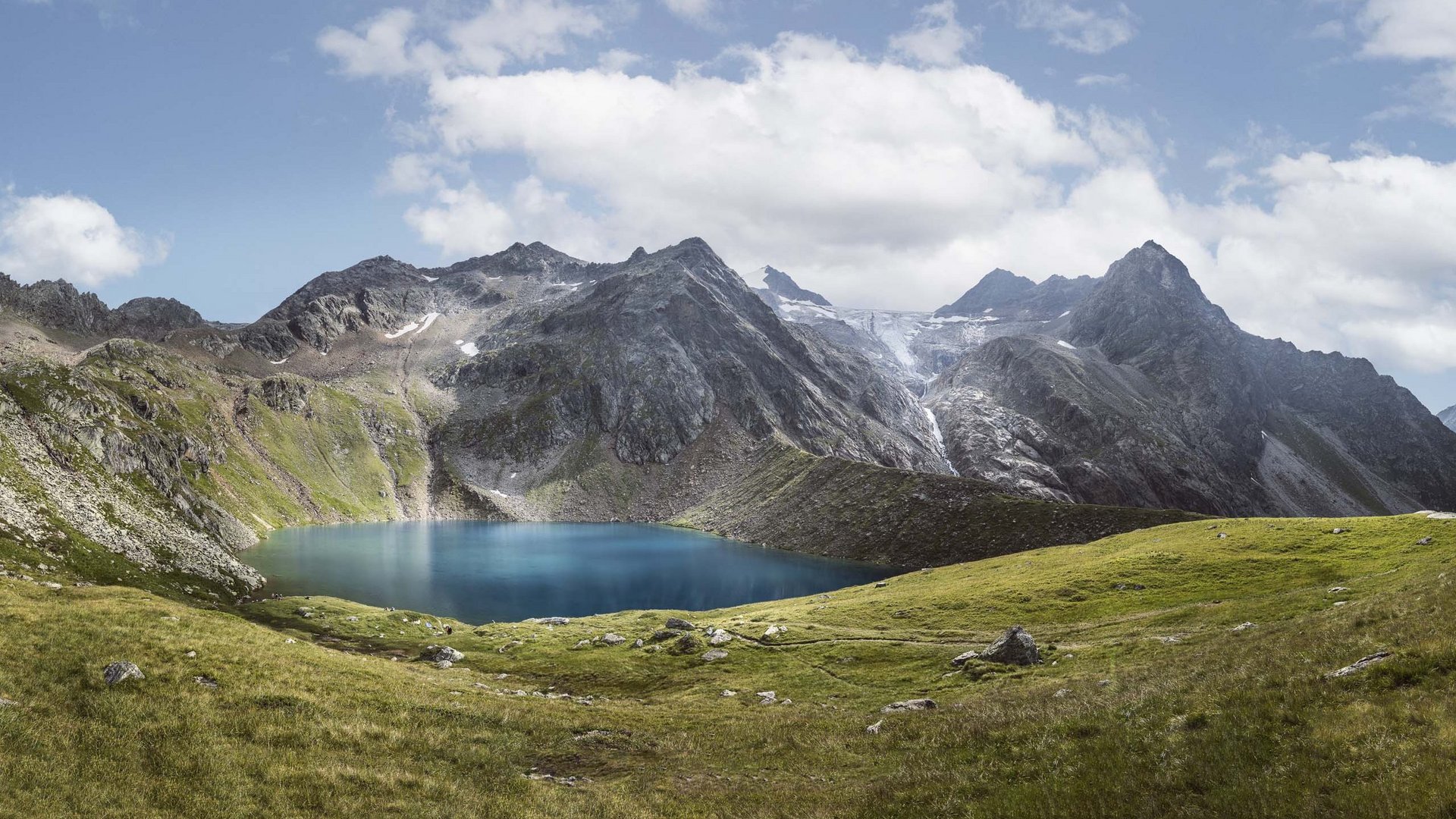 My Stubaital: a summer holiday at the Hotel Alphof Mountain lake surrounded by green meadows and rocky mountains under cloudy sky