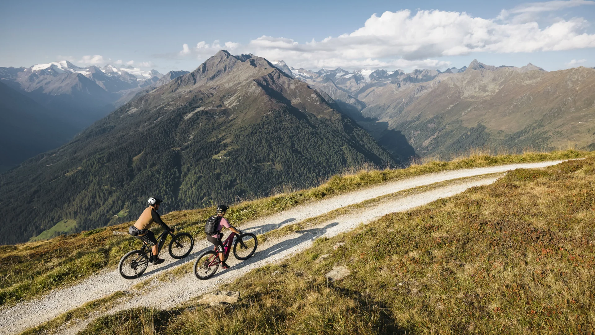 Two mountain bikers on a mountain trail overlooking the Alps