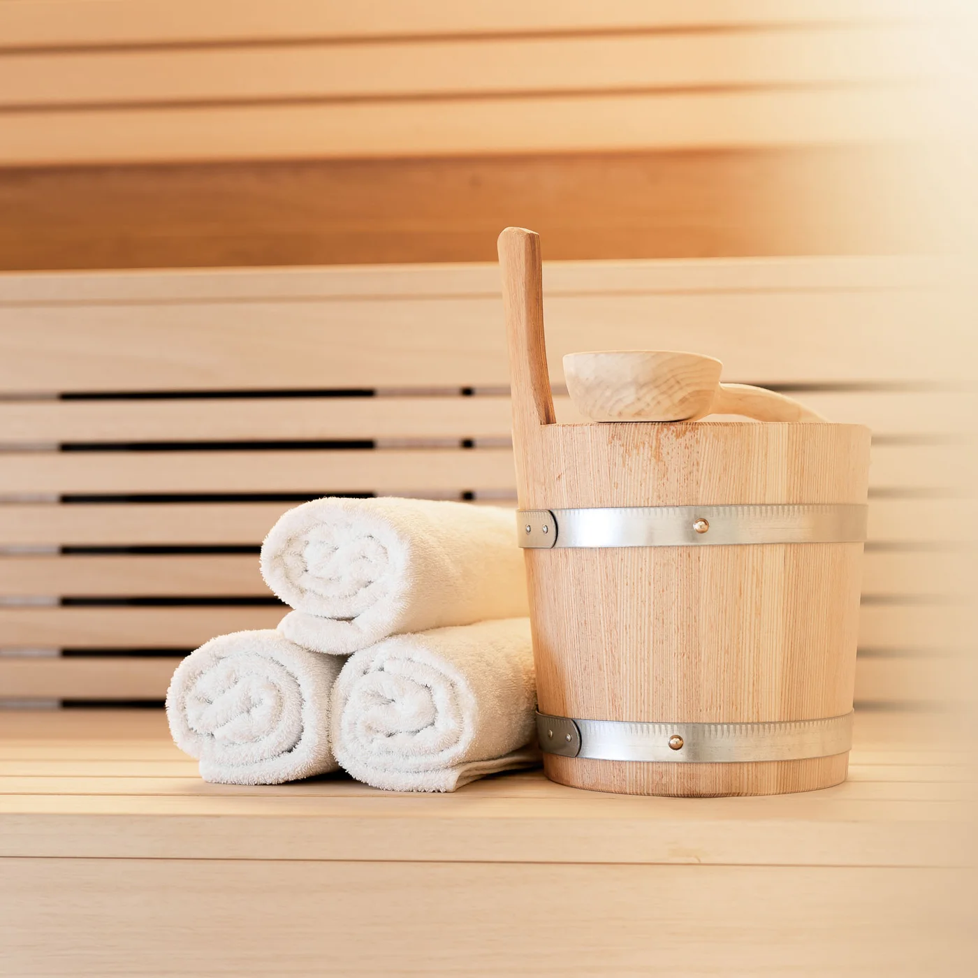 The modern AlpSpa at your spa hotel in Tyrol Sauna bucket with ladle and three rolled white towels on a wooden bench