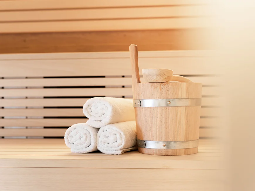 The modern AlpSpa at your spa hotel in Tyrol Sauna bucket with ladle and three rolled white towels on a wooden bench